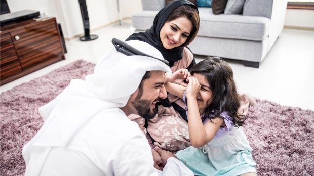 A happy Emirati family spending time together at home, symbolising the importance of financial protection and group life insurance in the UAE.